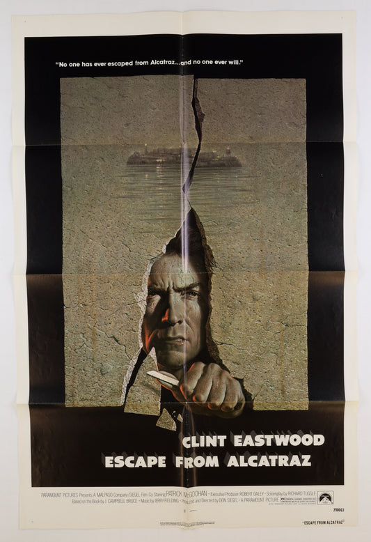 Front of an original 1979 U.S. one sheet movie poster for Escape from Alcatraz, featuring Clint Eastwood breaking through a cracked concrete wall with Alcatraz Island visible in the background.

