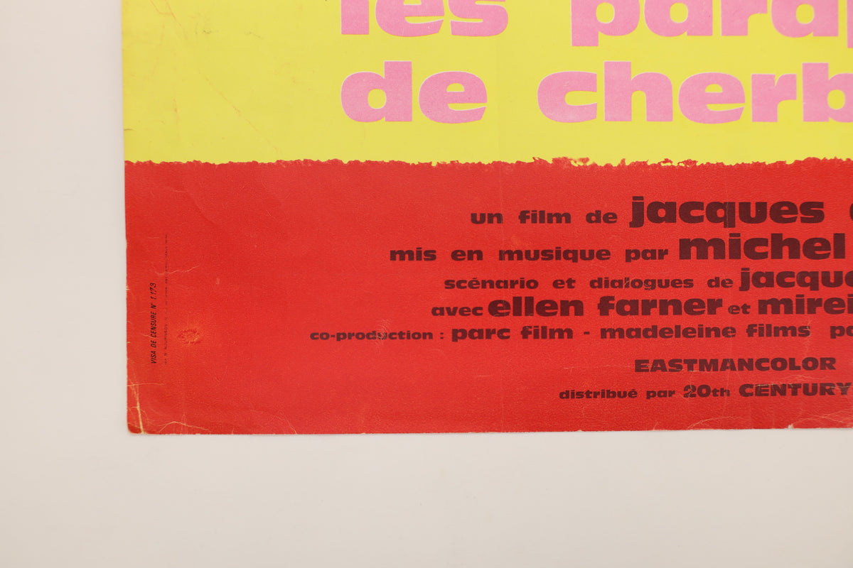 Detail of The Umbrellas of Cherbourg French poster showing lower-left edge wear, creasing and the printed distributor information.